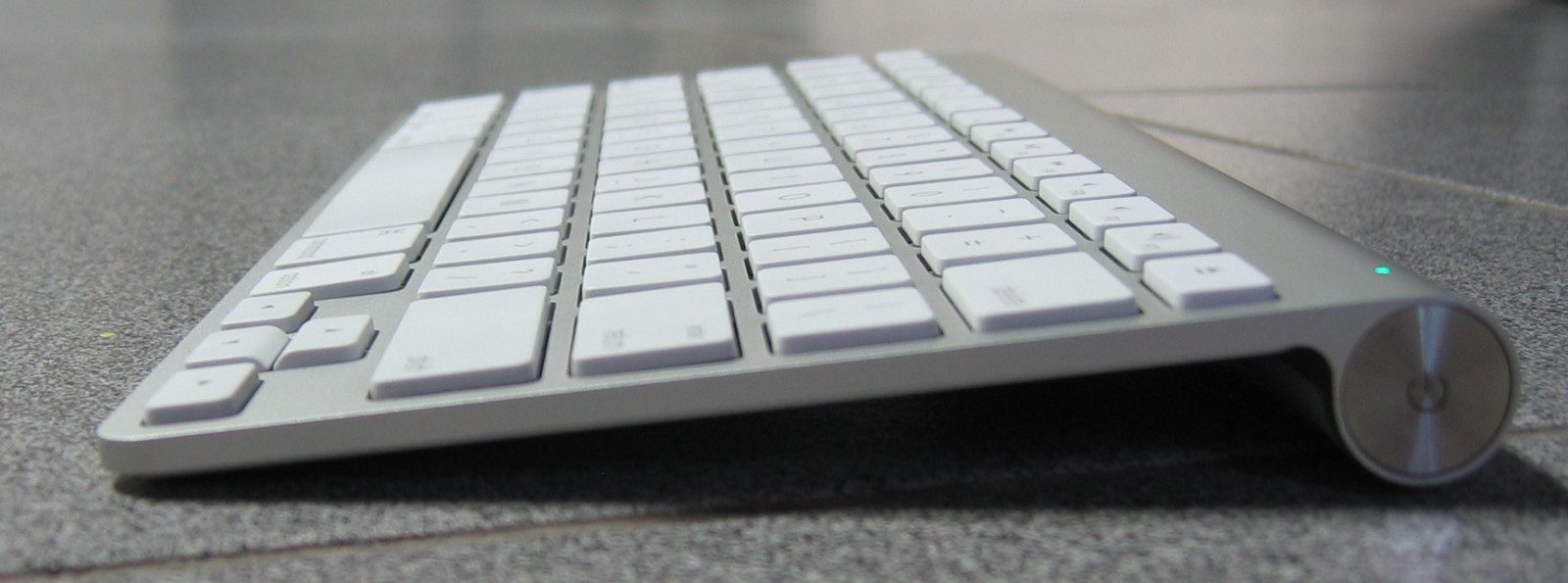 The end of an Apple Wireless Keyboard. A round slotted cap unscrews to reach the AA batteries.