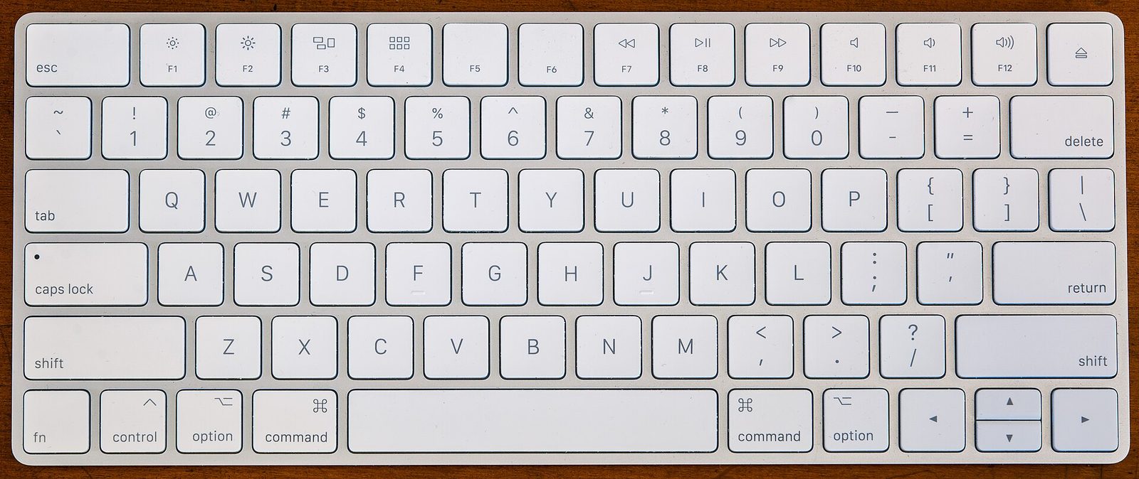 An Apple wireless keyboard seen straight down from above: low-profile white keys, no numeric keypad, and no port or cable in the picture.