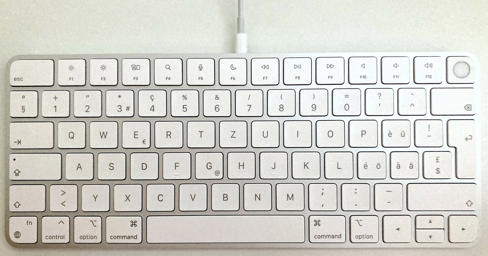 The top of a compact Magic Keyboard, Swiss layout. Right of F12 sits a plain round key with no symbol printed on it.
