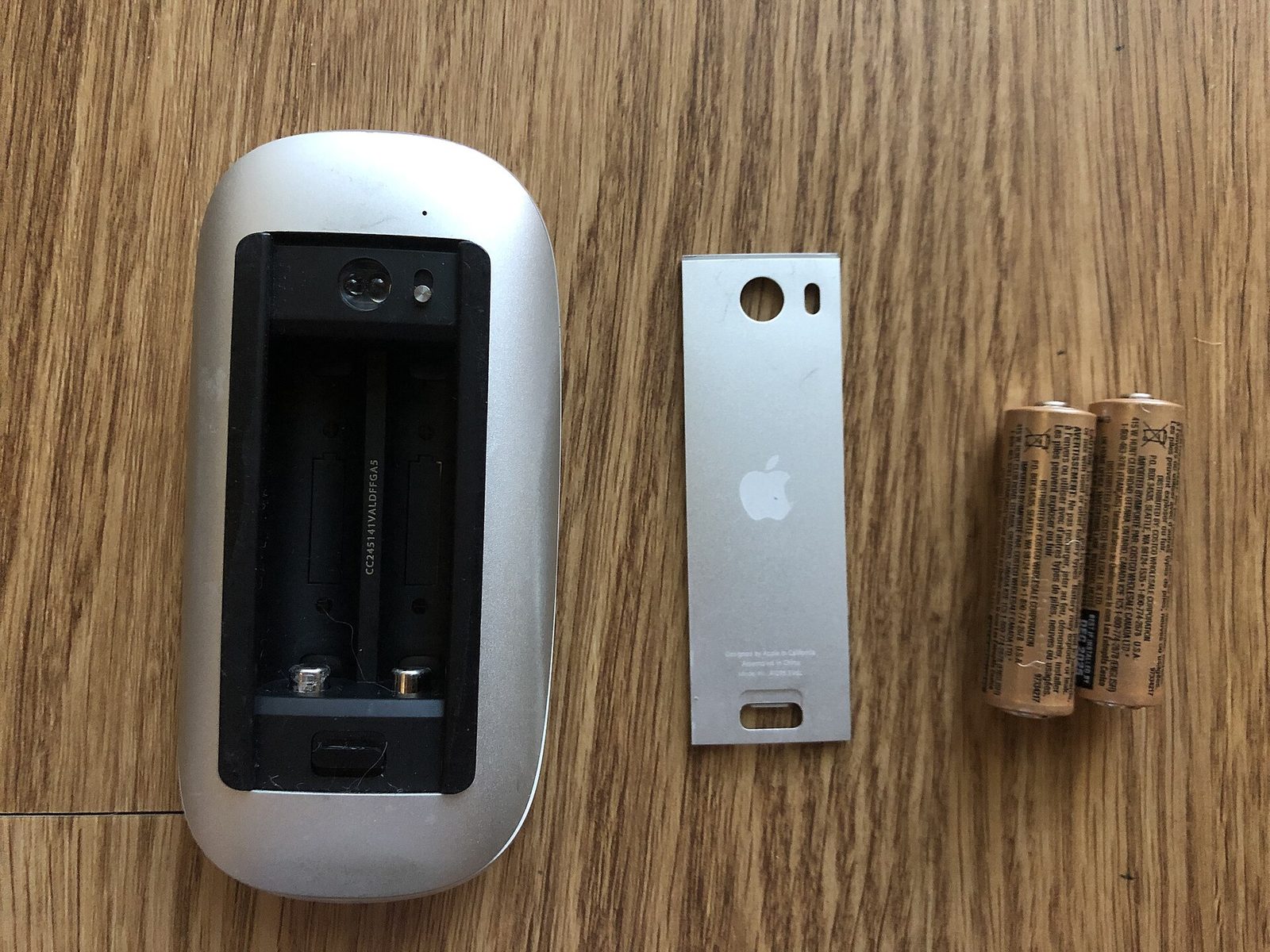 A Magic Mouse v1 with the battery door lifted off, showing the bay for two AA batteries.