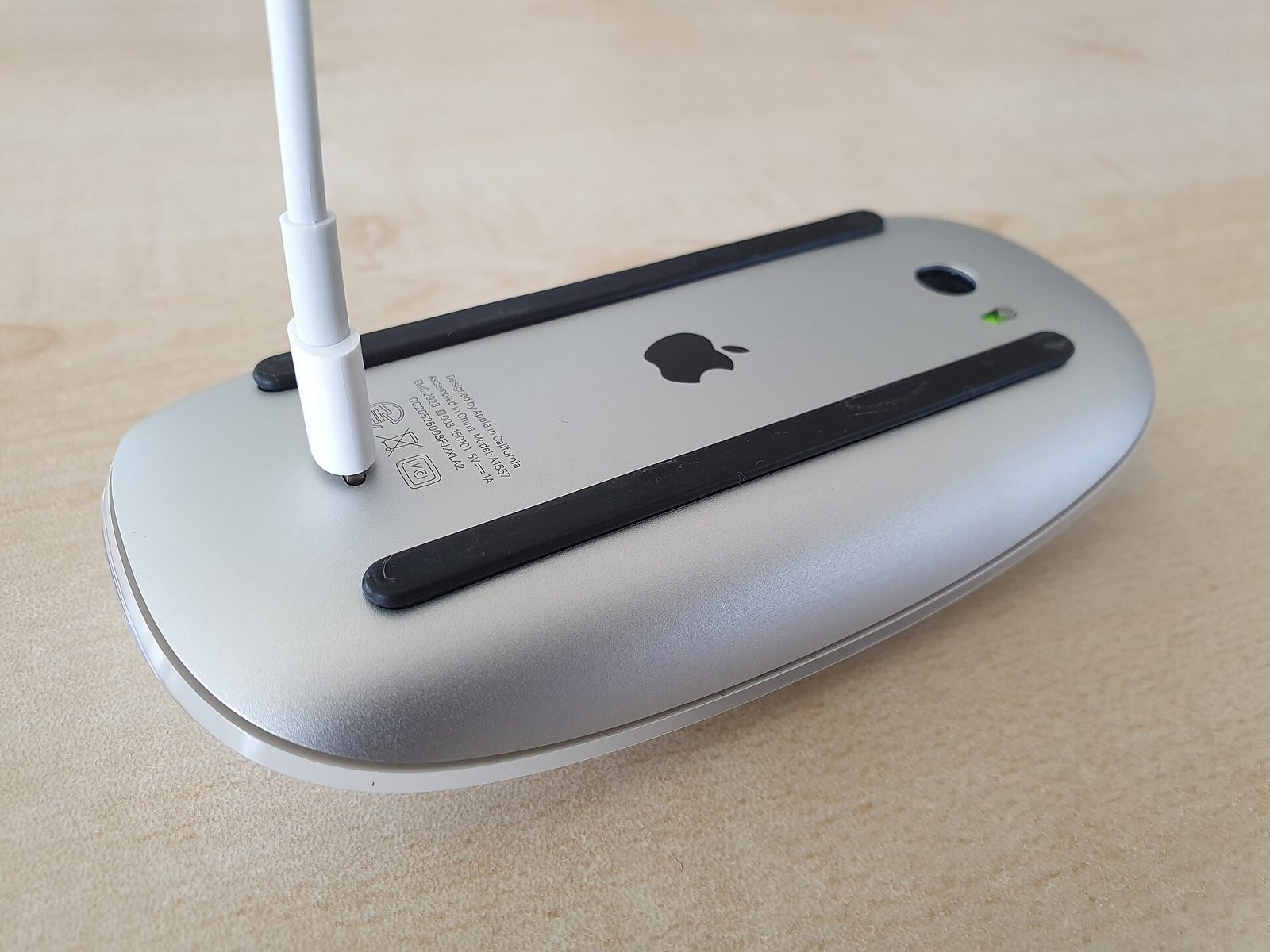Underside of a Magic Mouse v2. There is no battery door. A cable plugs into a port on the bottom, and the etched text reads Model A1657.