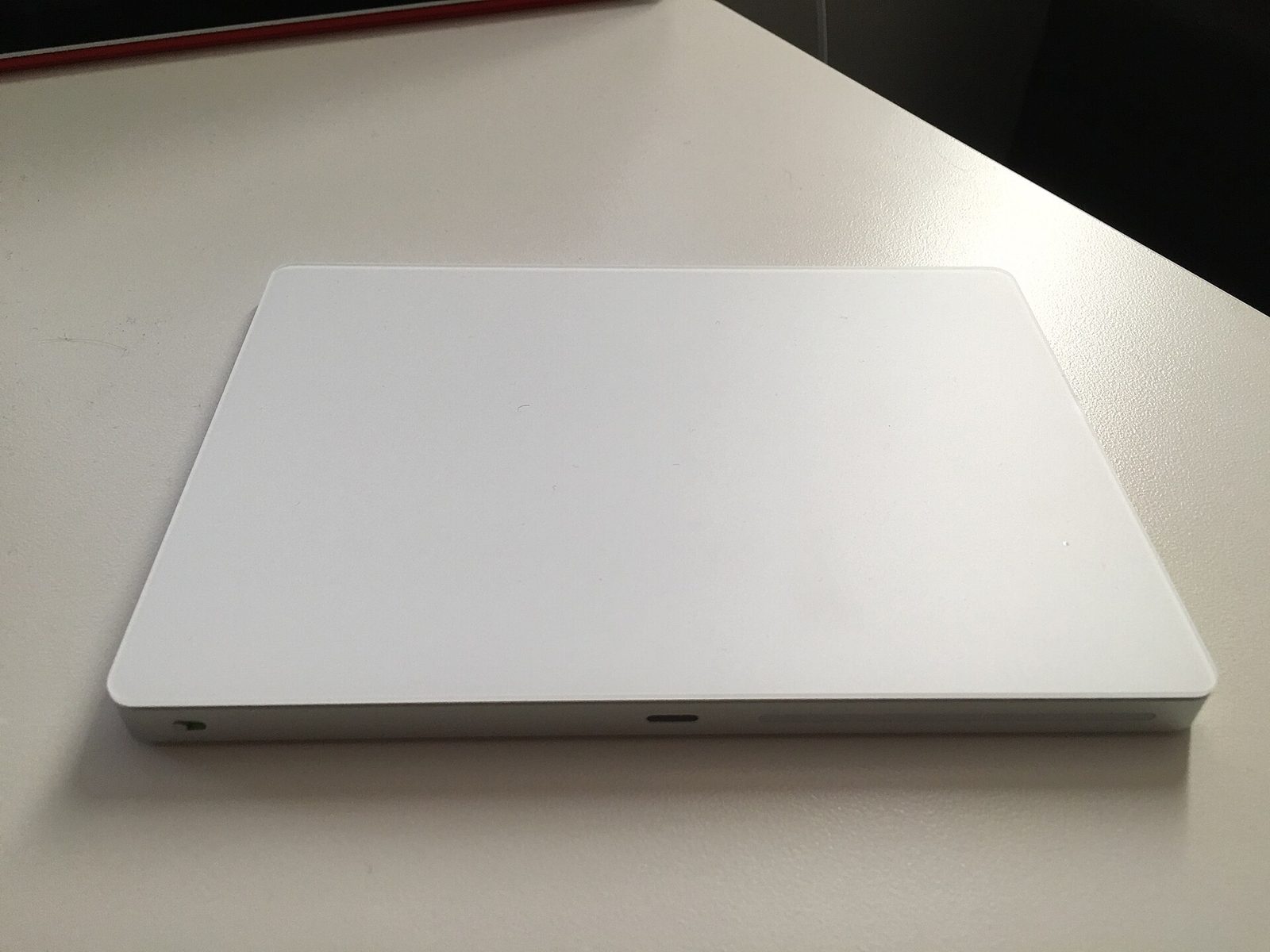 A rechargeable Magic Trackpad, seen from the front. A small port sits in the middle of the near edge.