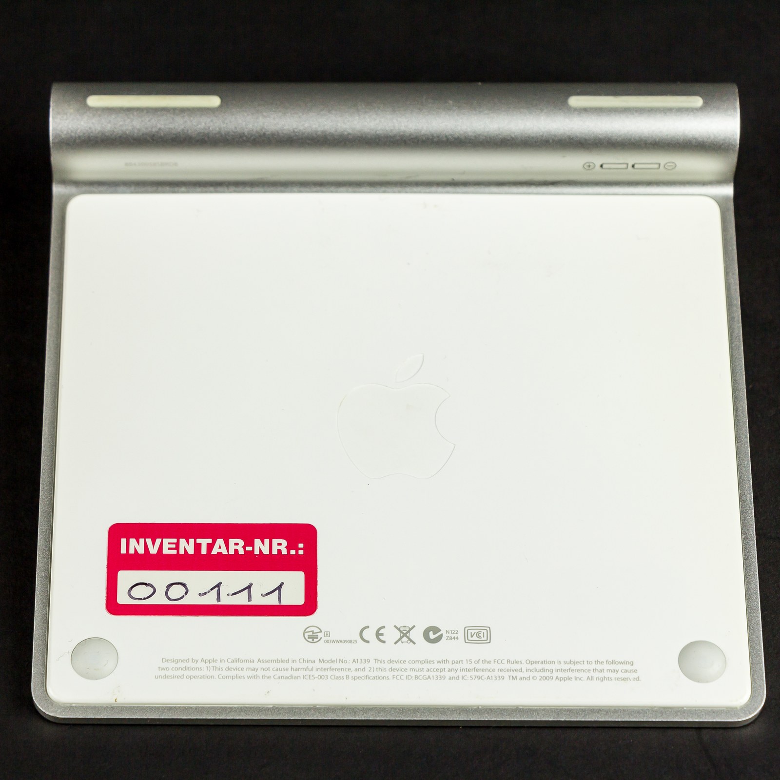 Underside of a Magic Trackpad from 2010, beside its aluminium battery tube. The small print reads Model No.: A1339.